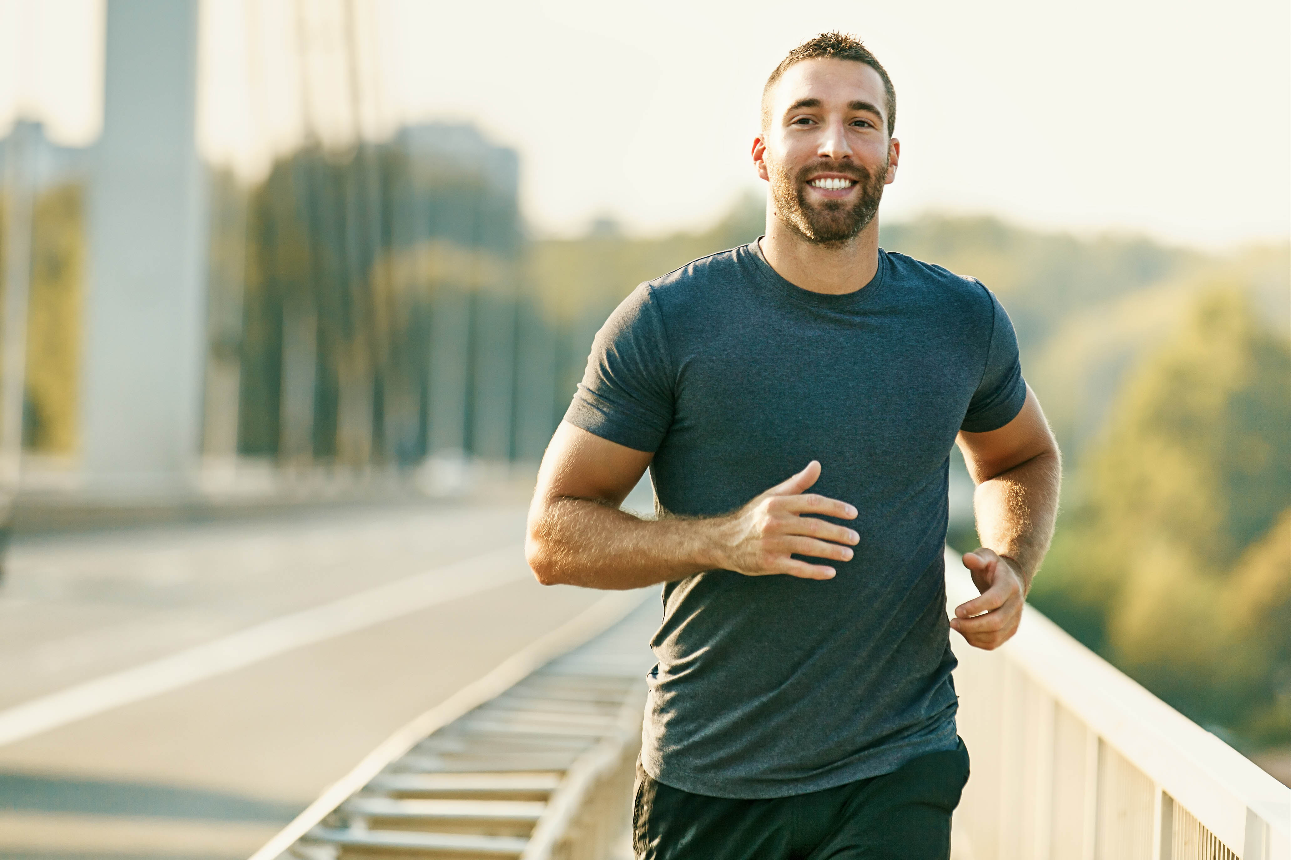 Young fit man, smiling and running along a bridge in the spring/summer